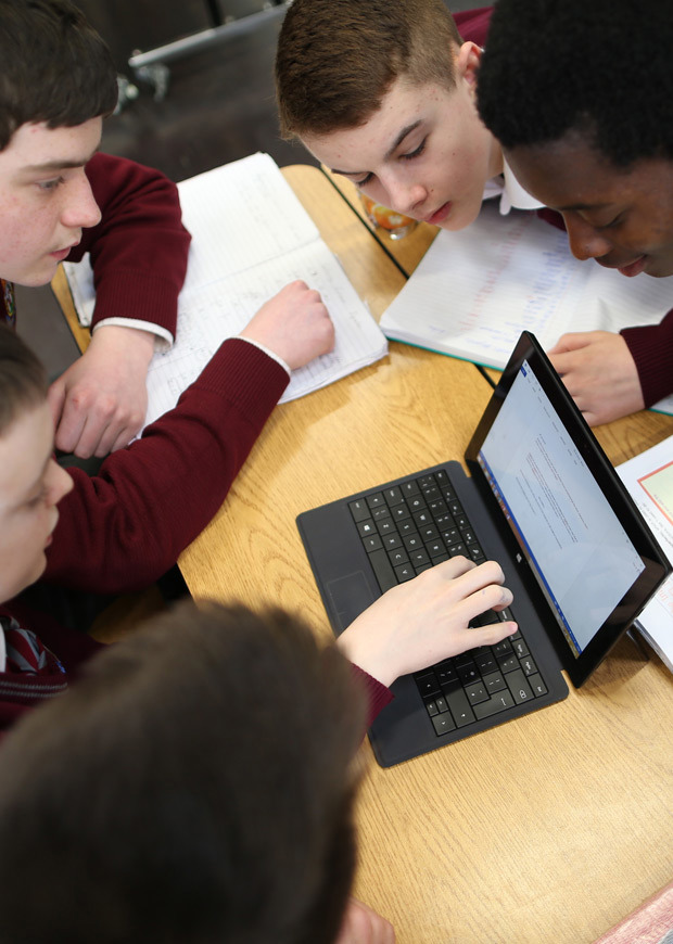 Group of students working together and looking at a laptop, portrait crop