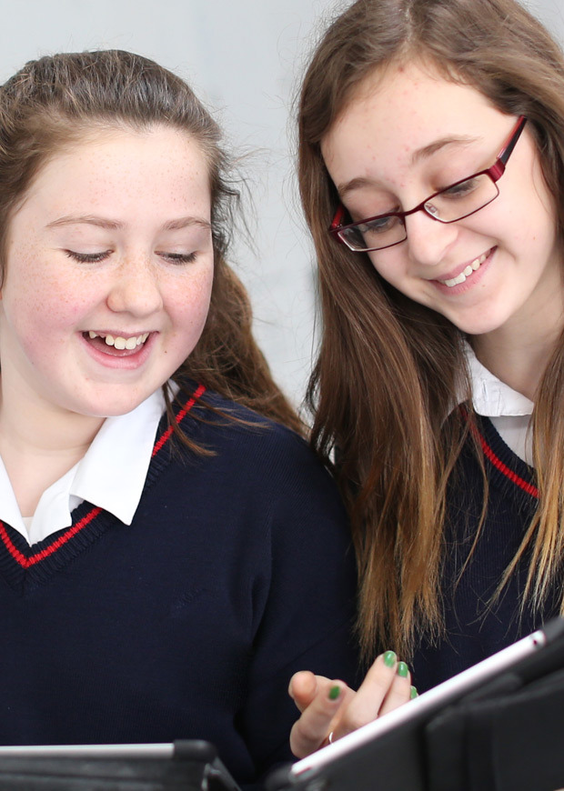 Close up of two students smiling and looking at iPads in the school corridor