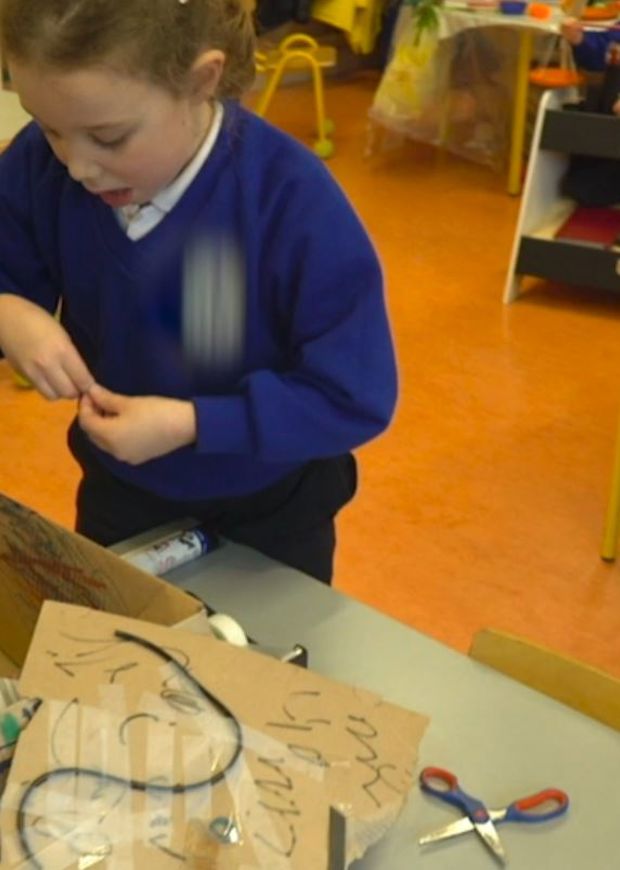 Three children creating artwork with cardboard in class