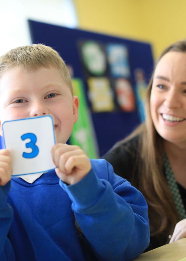 Child holding up number card with teacher