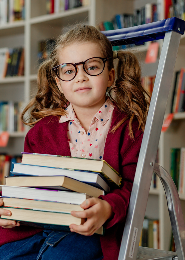 Young child holding books while seated on a library ladder